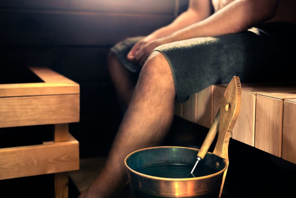 Man sitting in the sauna with a bucket ready to throw it on the stones for an authentic sauna experience