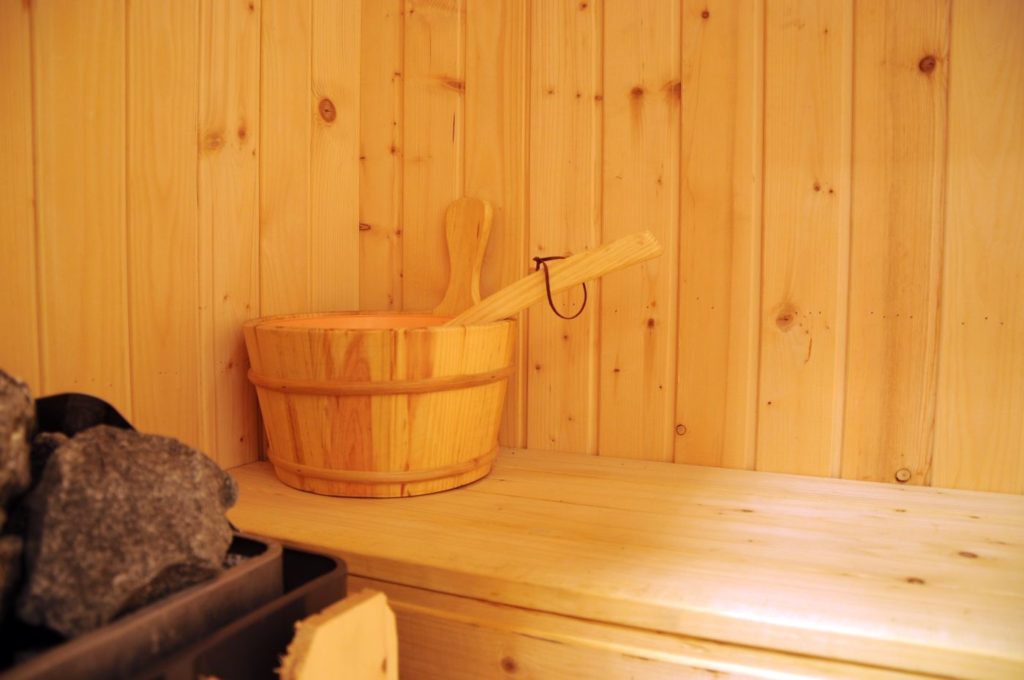 A wood burning stove with water thrown on it from wooden bucket creates löyly